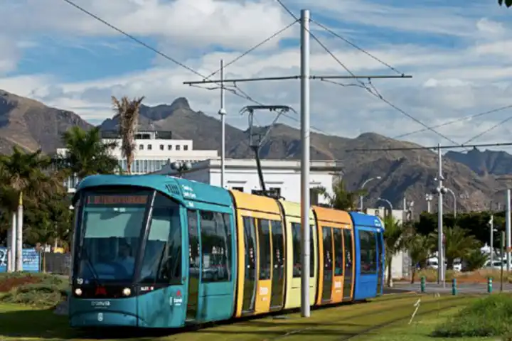 Tram van Tenerife tegen slechte geuren - Tram rijdt in stedelijke omgeving met bergen.