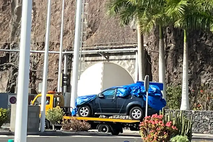 Ongeval veerboot Tenerife - Beschadigde auto op takelwagen naast palmbomen.